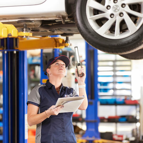 Automotive technician inspecting car underneath vehicle lift in repair shop