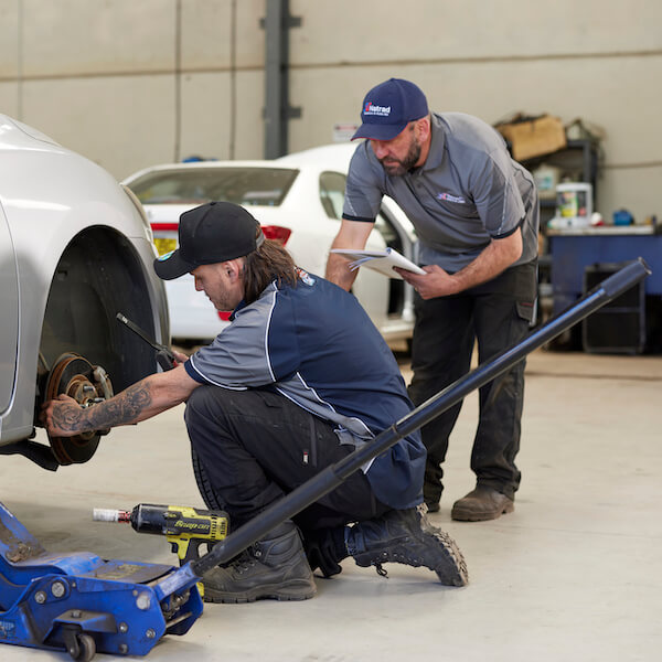 Two mechanics working on a car in an automotive repair shop