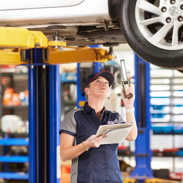Auto mechanic inspecting vehicle undercarriage on hydraulic lift