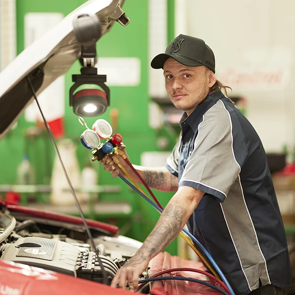 Mechanic with diagnostic tool working on car engine in auto repair shop