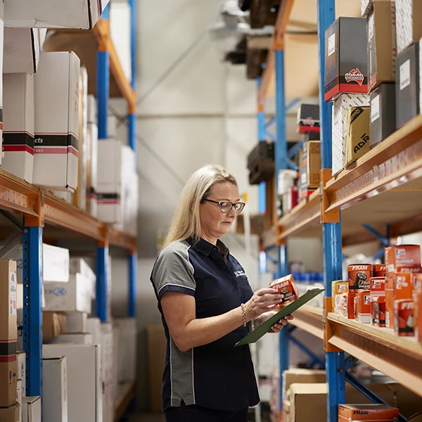 Warehouse worker checking inventory on shelves with clipboard