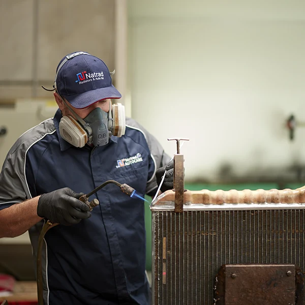 Worker wearing respirator and gloves repairs industrial radiator