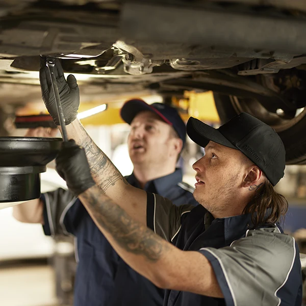 Mechanics inspecting car undercarriage with flashlight in auto repair shop