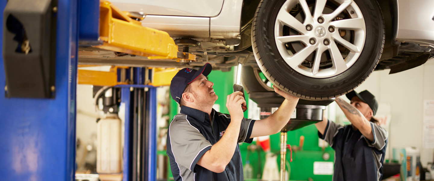 Mechanic inspecting car underside using flashlight in auto repair shop