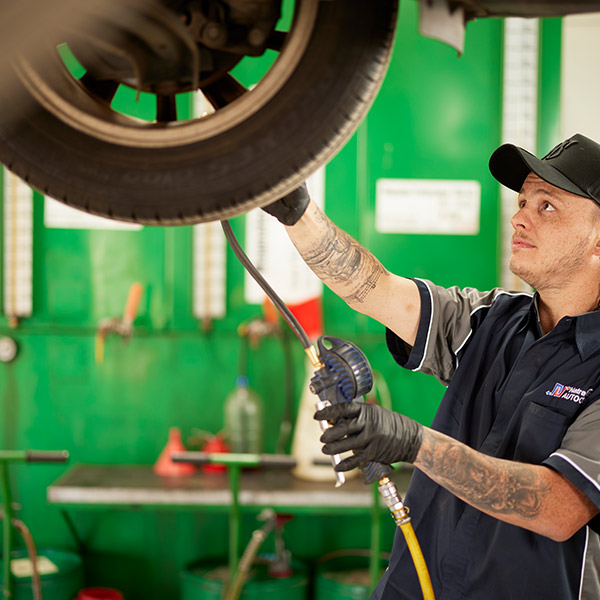 Mechanic balancing tire on machine in green automotive workshop