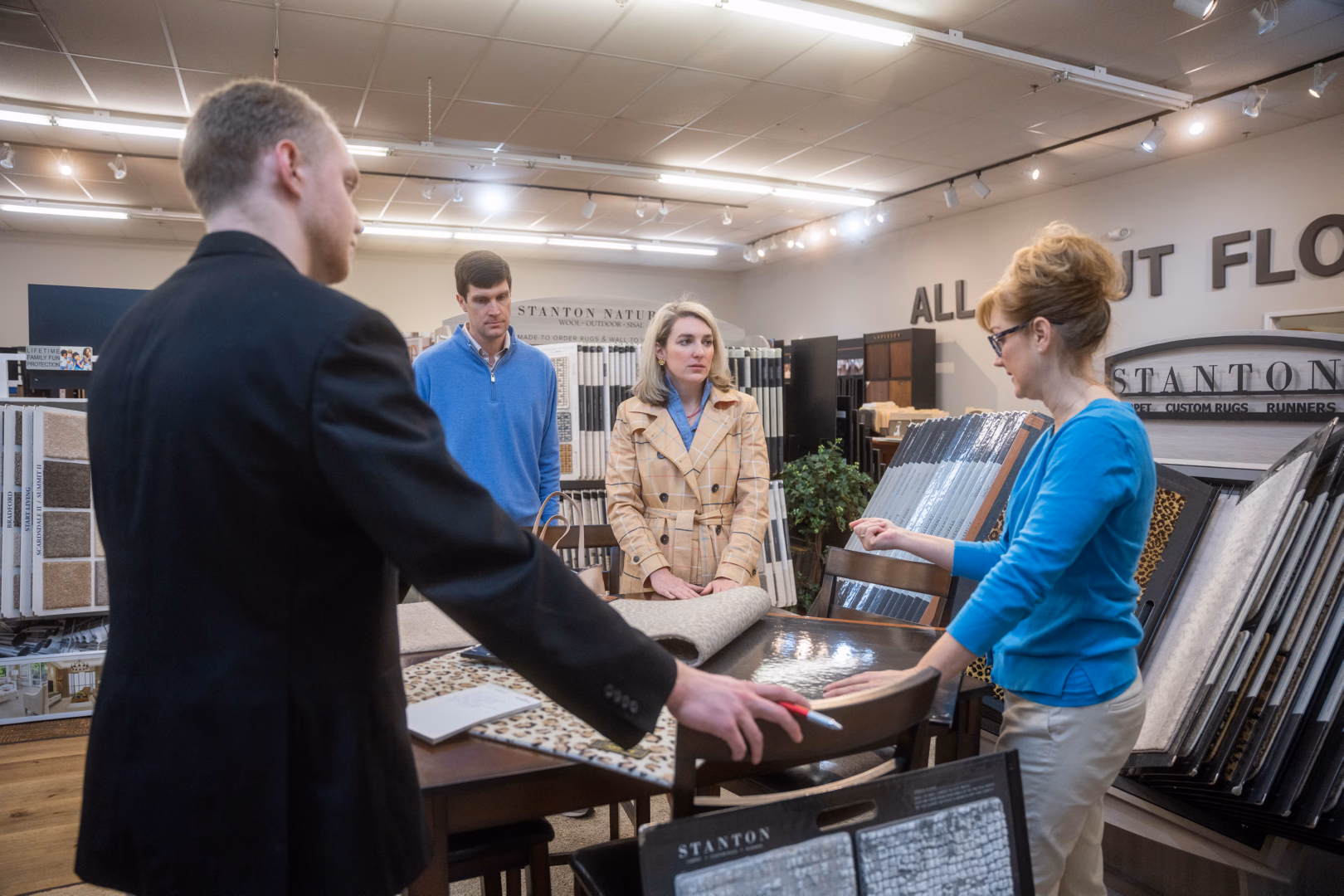 Four people in a flooring showroom examining carpet and rug samples on a table.