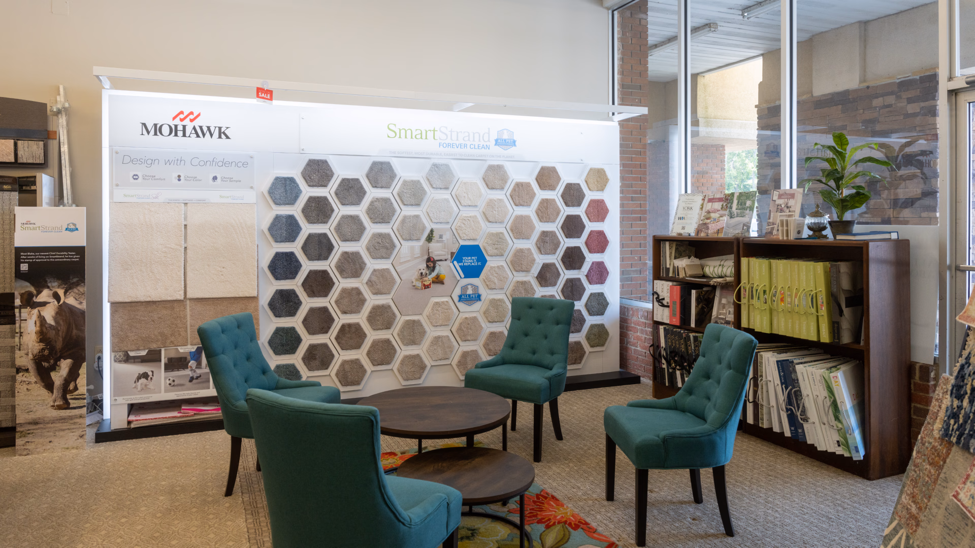 Showroom corner with teal upholstered chairs around round wooden tables and a wall display of hexagonal carpet samples in various colors.