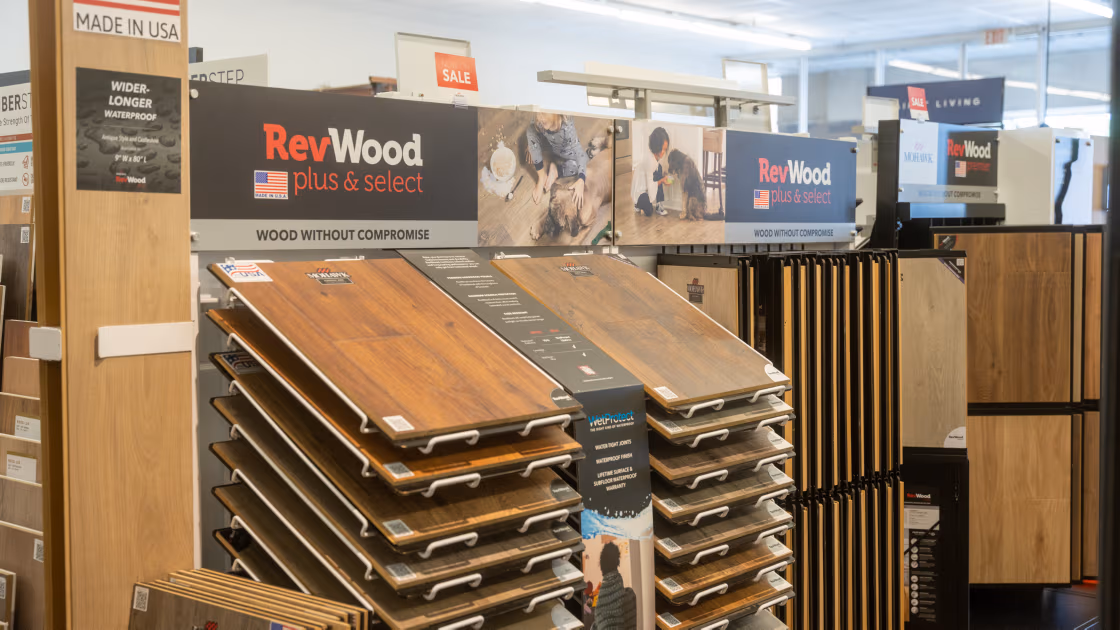 Indoor showroom display of RevWood plus & select wood flooring samples with various wood finishes and a 'Made in USA' label.
