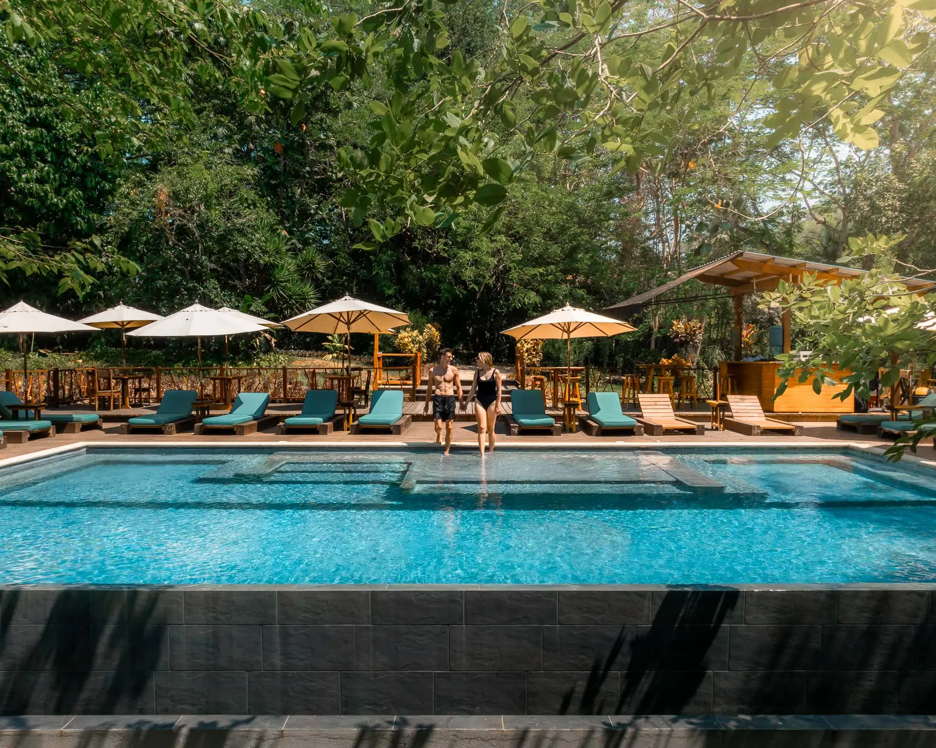 A couple walking at the edge of the clear blue jungle-view infinity pool at Sweet Songs Jungle Lodge in Belize.