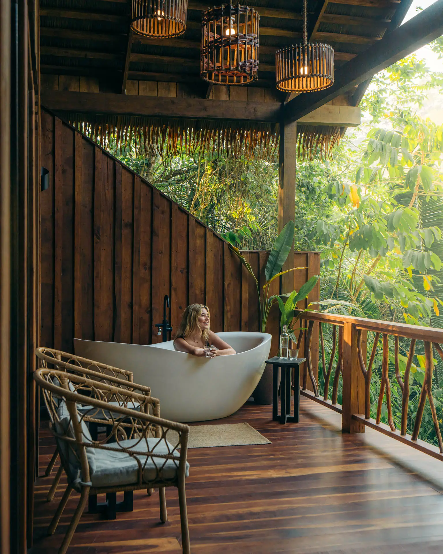 Woman relaxing in a white outdoor bathtub on a wooden balcony of the signature treehouse suite at Sweet Songs Jungle Lodge in Belize.