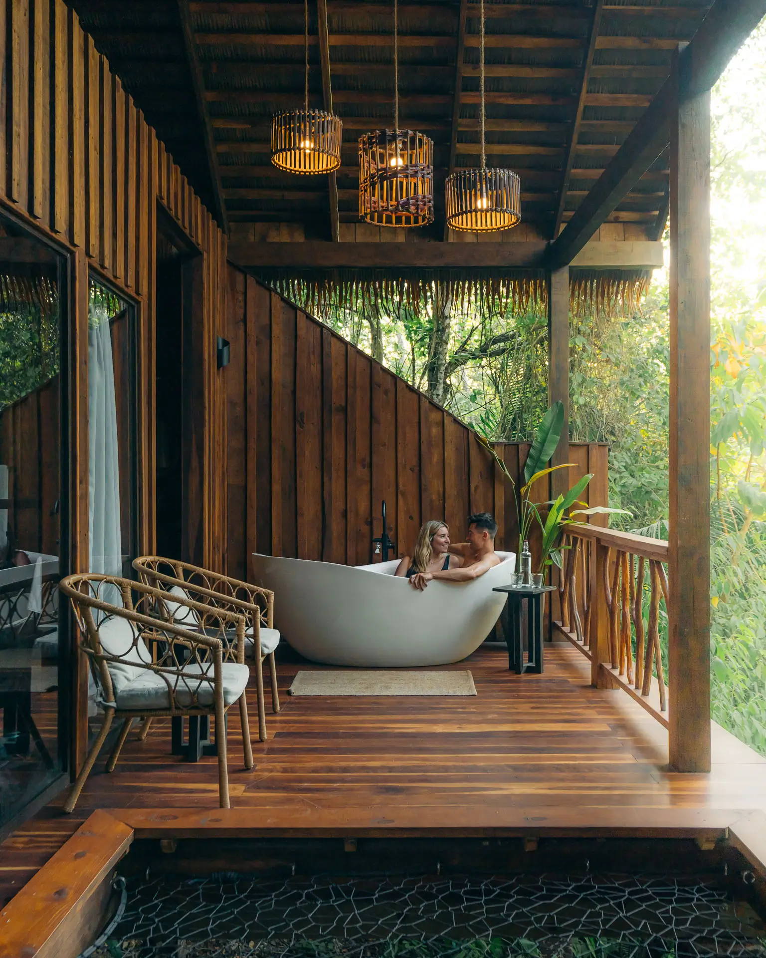 Couple relaxing together in an outdoor bathtub on a wooden jungle lodge balcony at Sweet Songs Jungle Lodge in Belize.