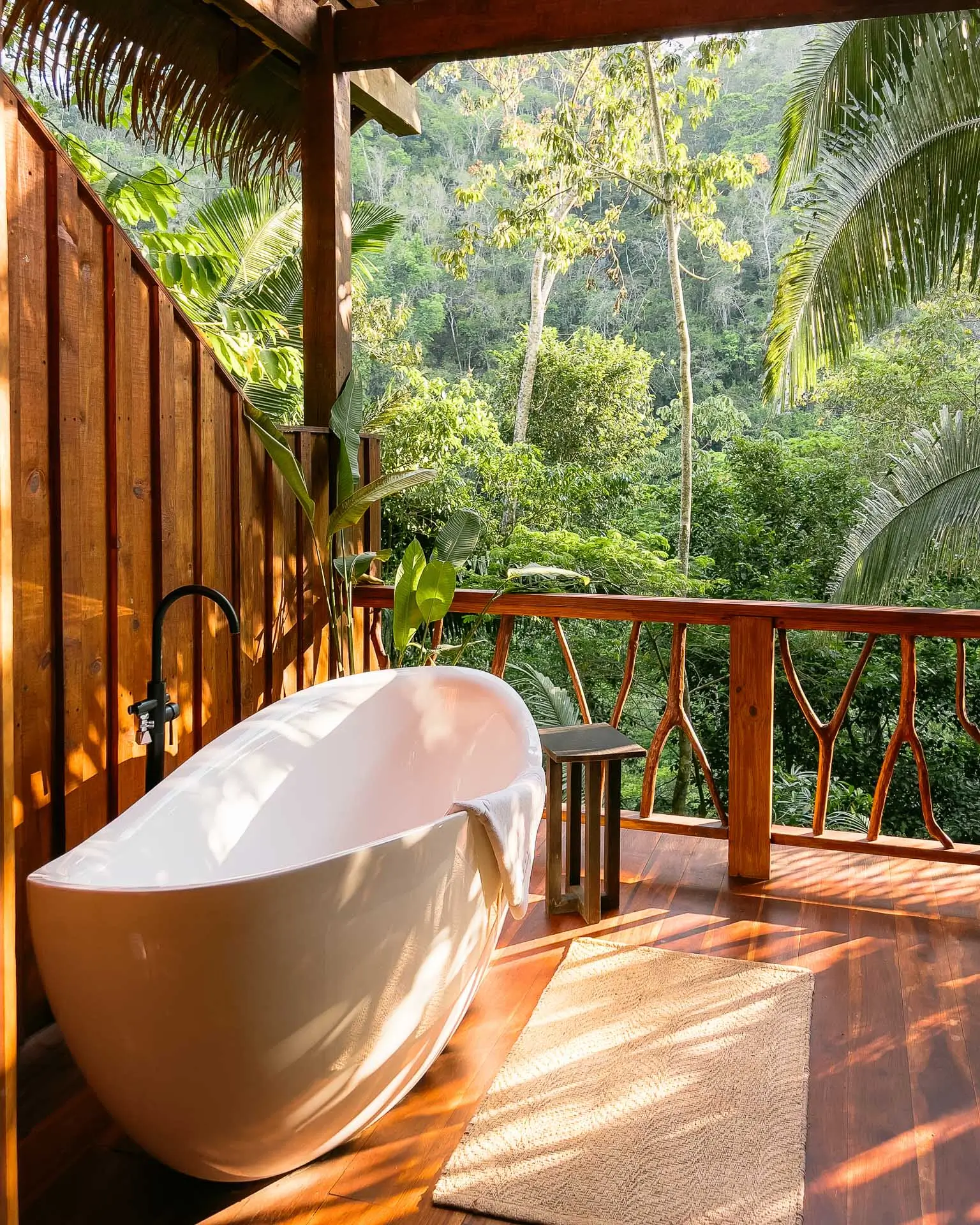 Outdoor bathtub on wooden deck surrounded by tropical plants and forest view at Sweet Songs Jungle Lodge in Belize.