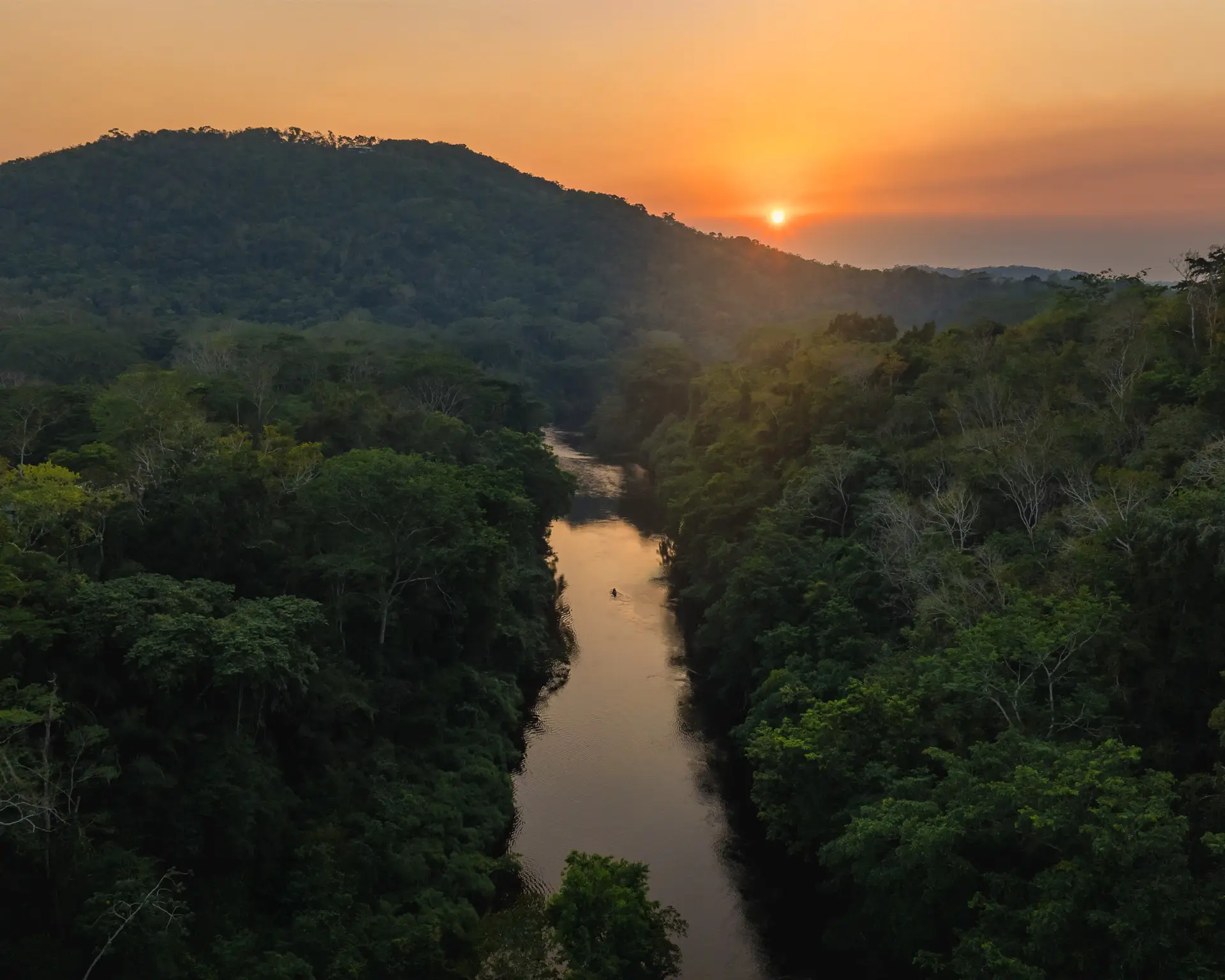 Sunset over the Macal River flowing through dense jungle with a small canoe in the water at Sweet Songs Jungle Lodge in Belize.