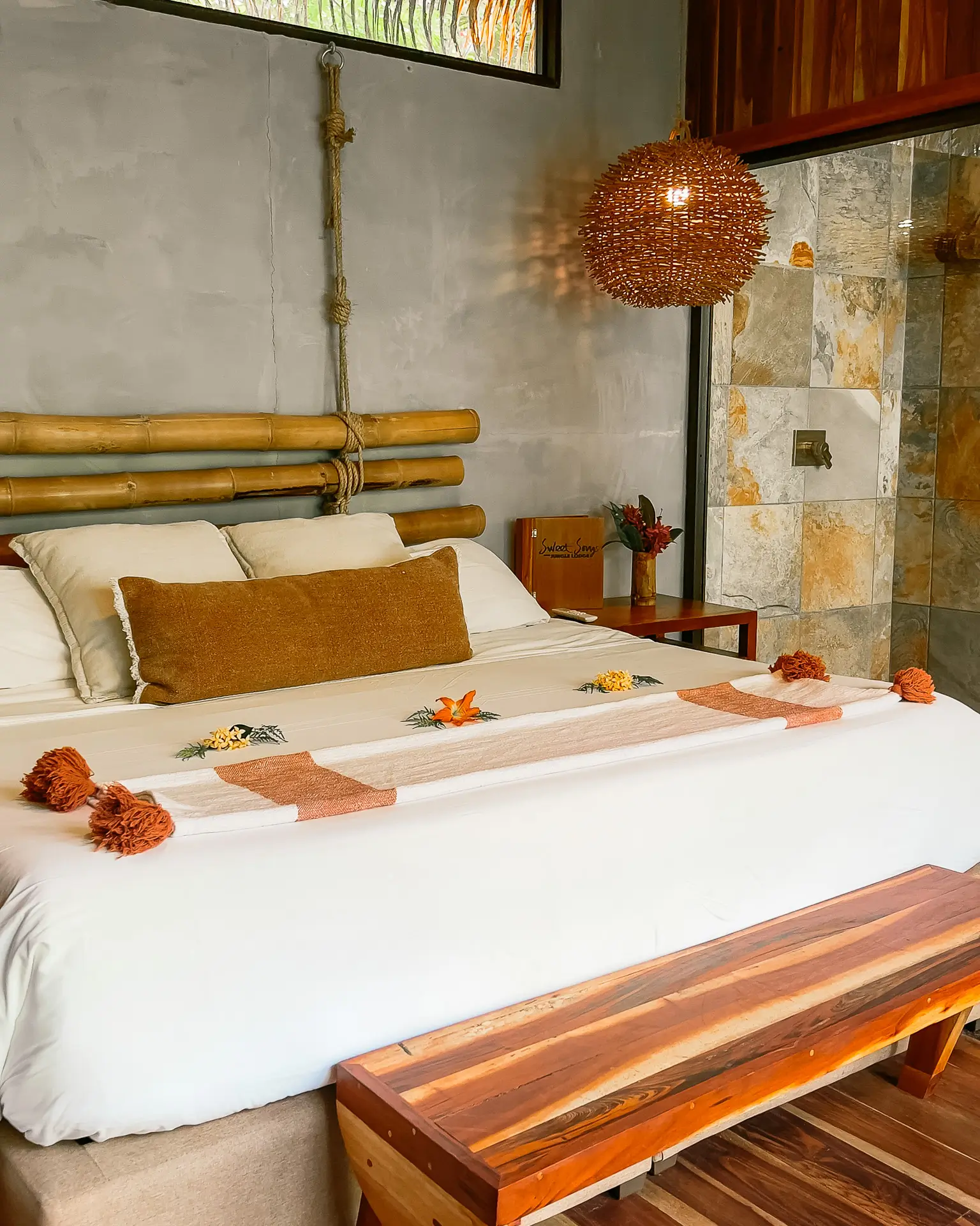 Signature Treehouse Suite bedroom at Sweet Songs Jungle Lodge in Belize with bamboo headboard, warm decor, and tropical flowers on the bed.