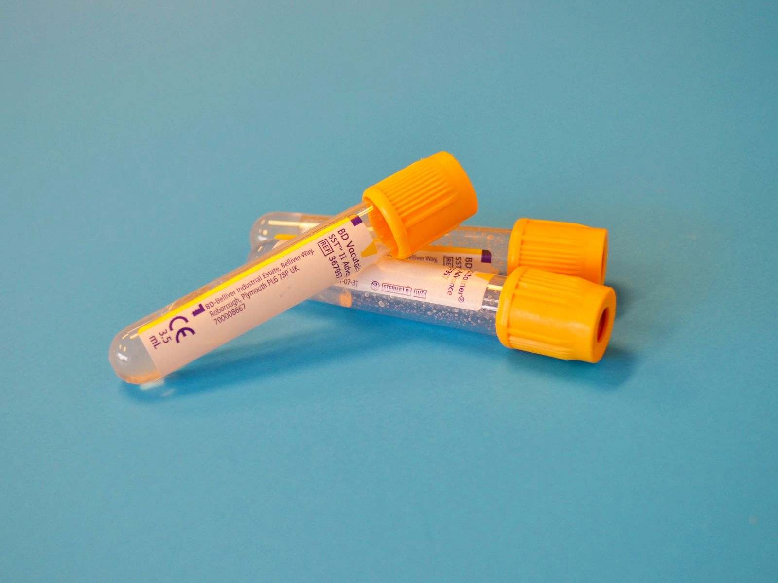 Two collection tubes with orange caps on a blue surface