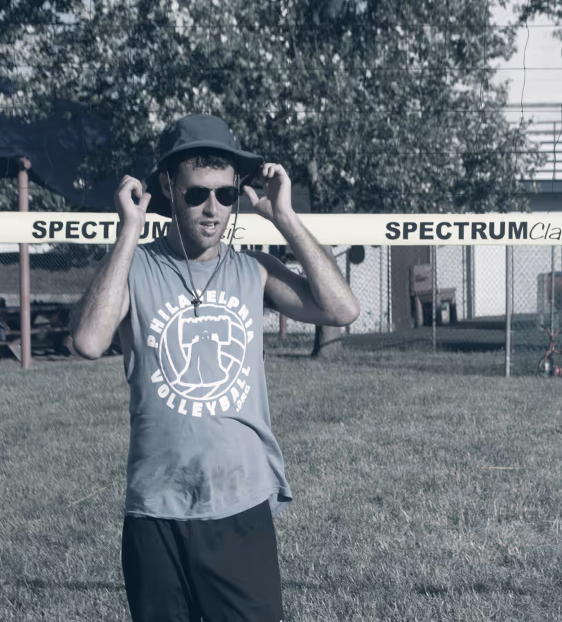 Jeremy in a hat outside in front of a volleyball net.
