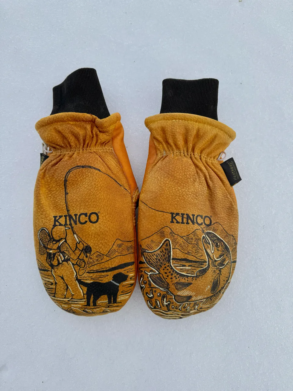 Pair of brown Kinco mittens with fishing-themed illustrations, one showing a fisherman and dog, the other a jumping fish.