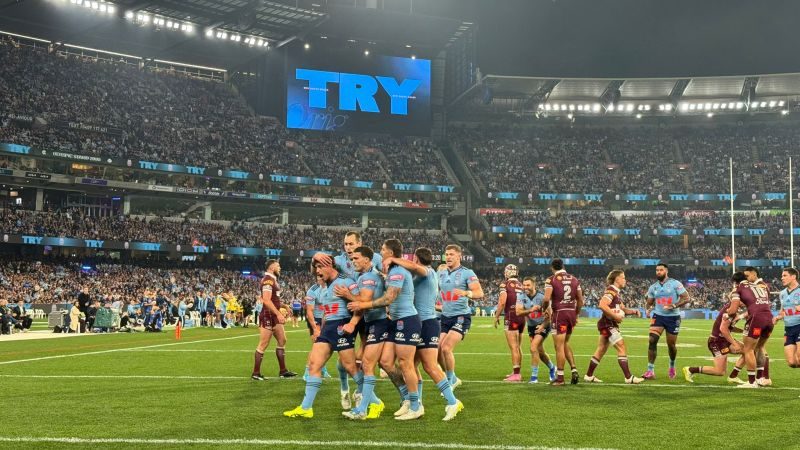 NSW players celebrate a try at State of Origin with the big screen behind