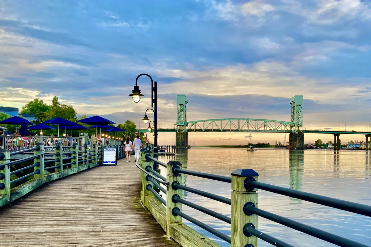 The Wilmington Riverwalk along the Cape Fear River at sunset, with the Cape Fear Memorial Bridge in the distance
