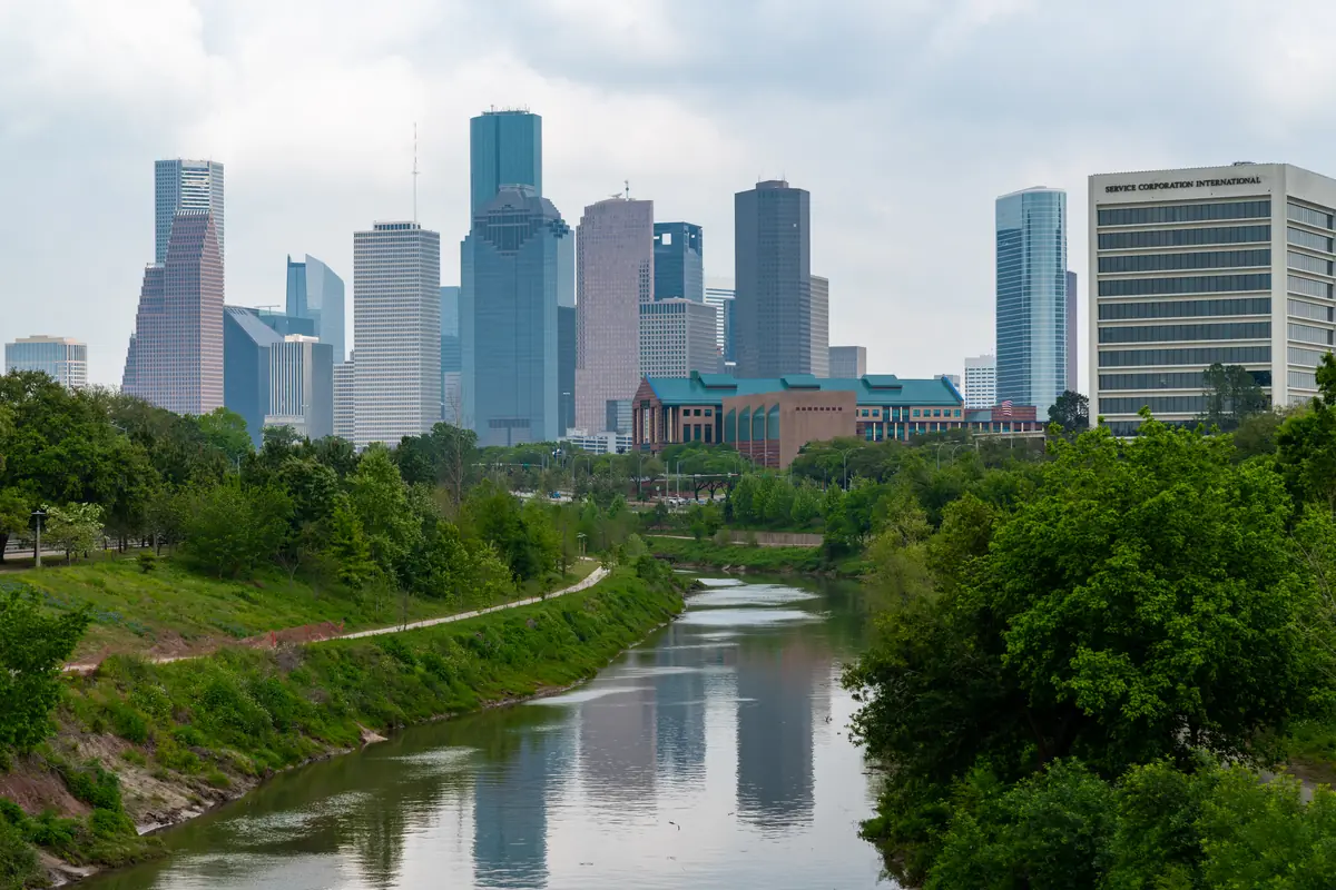 Downtown Houston skyline seen from the Rosemont Bridge over Buffalo Bayou, with trees in the foreground