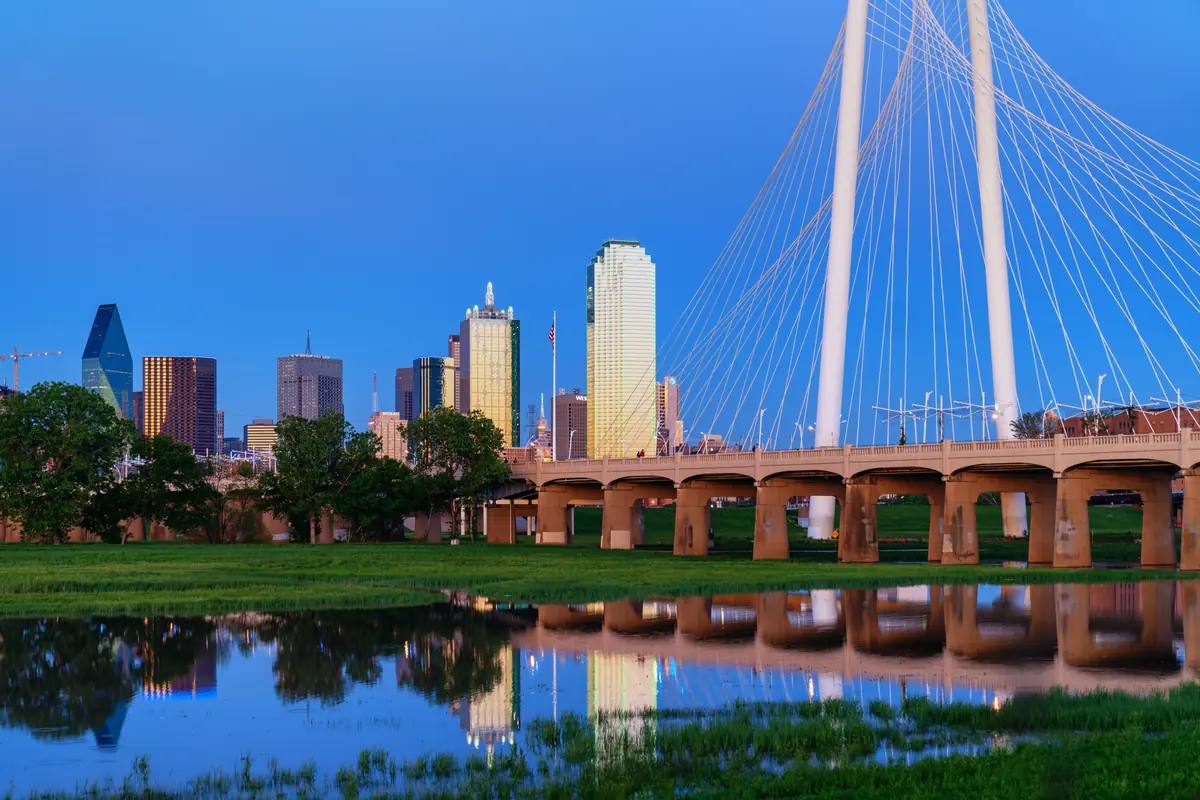 Downtown Dallas skyline beyond the Trinity River and the white arch of the Margaret Hunt Hill Bridge