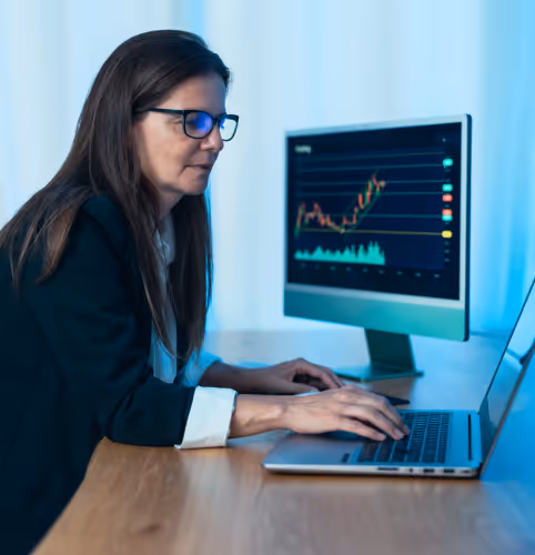 Business professional with glasses analyzing financial charts and data on computer monitors while working on laptop