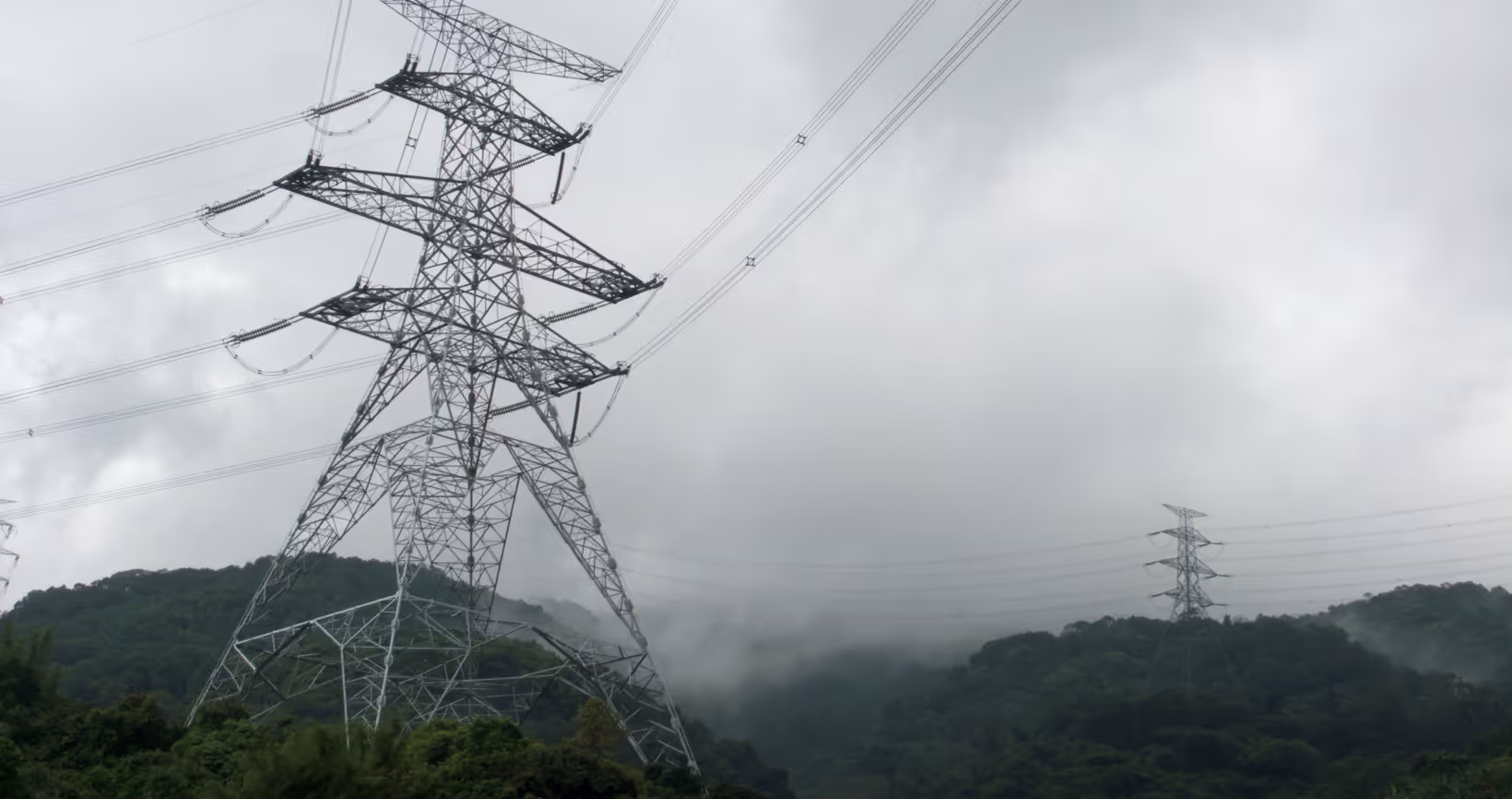 High-voltage electrical transmission tower with power lines in misty mountain landscape with forested hills