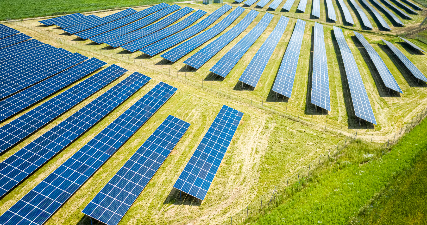 Aerial view of solar panel arrays arranged in rows across green farmland