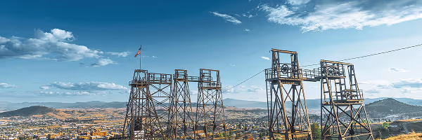 A panoramic view of industrial structures on a hilltop with an American flag flying, surrounded by a scenic landscape of mountains and plains - cropped