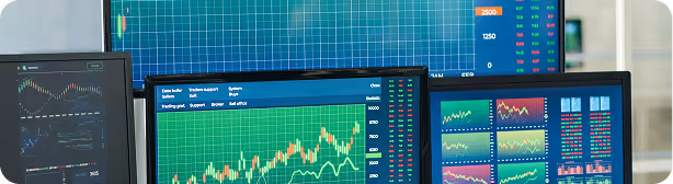 Multiple computer monitors displaying financial trading charts with green candlestick patterns and various market data visualizations