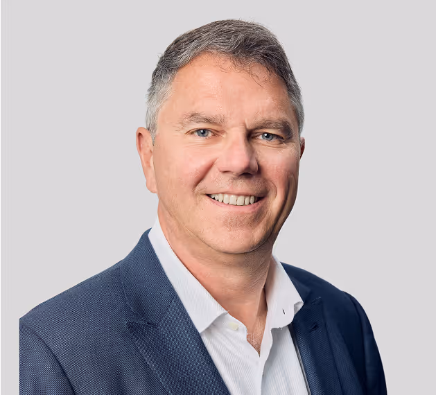 Professional headshot of smiling man with gray hair wearing navy blazer over white collared shirt