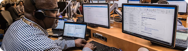 IT professional wearing headset working at desk with multiple computer monitors in office environment
