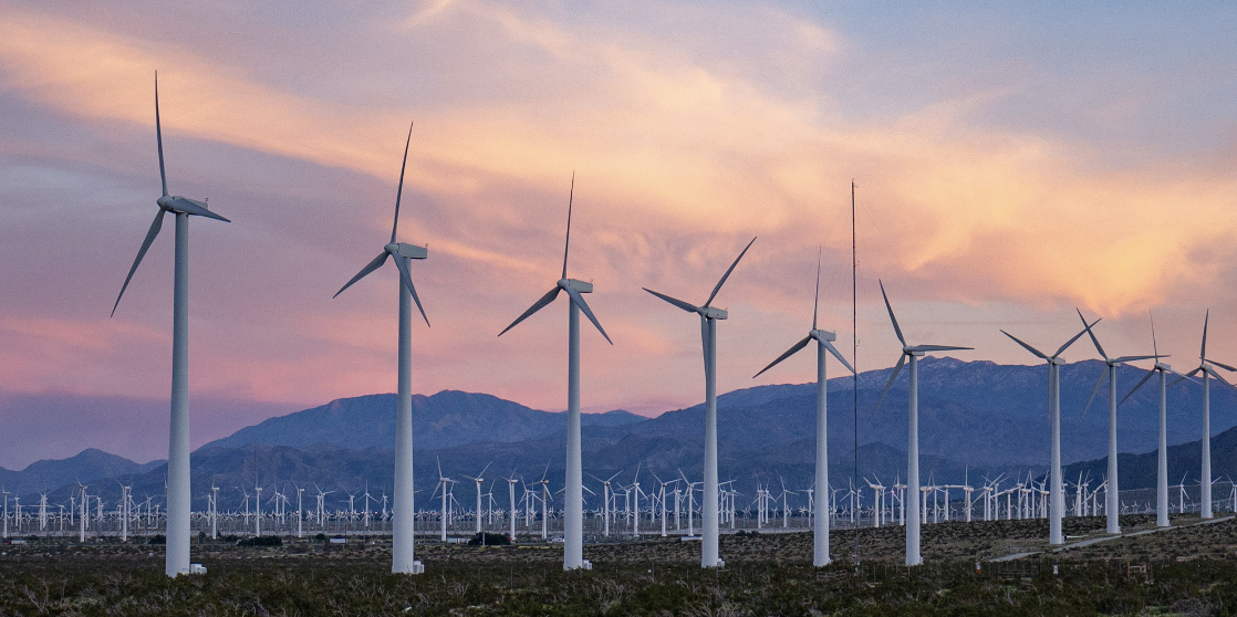 Wind turbine field with mountains and a sunset sky