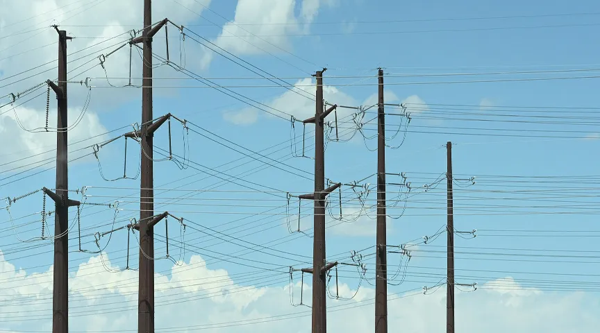 Multiple tall utility poles with interconnected power lines against a blue sky with clouds.