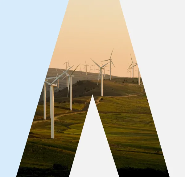 Wind turbines on rolling green hills under an orange sky at sunset.