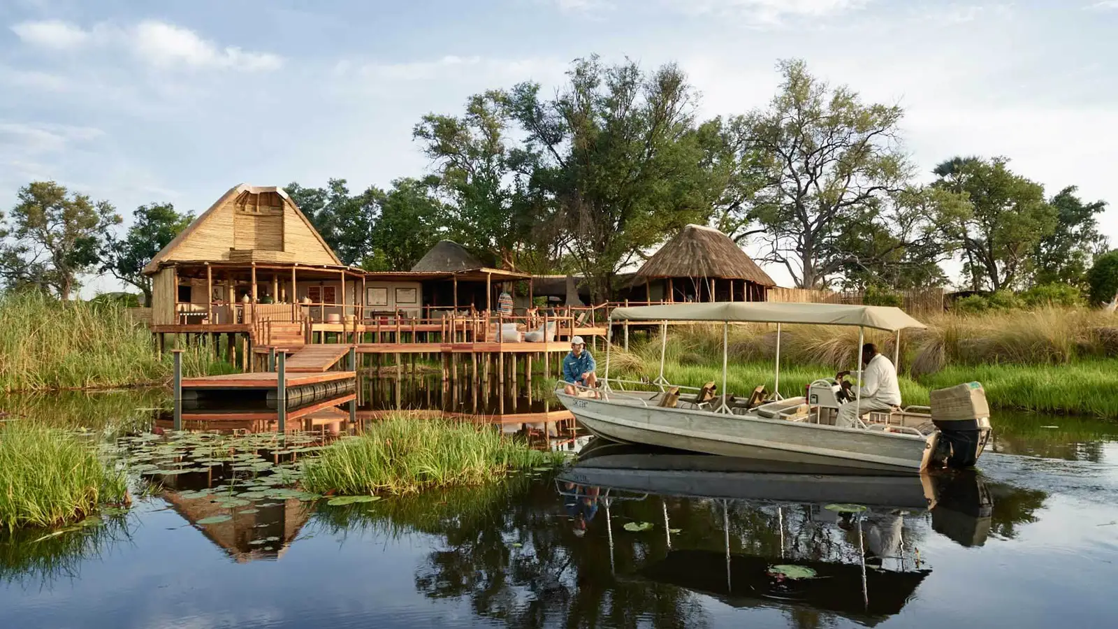 A motorboat approaches the luxury thatched-roof lodge on stilts for a Baines Camp River Arrival