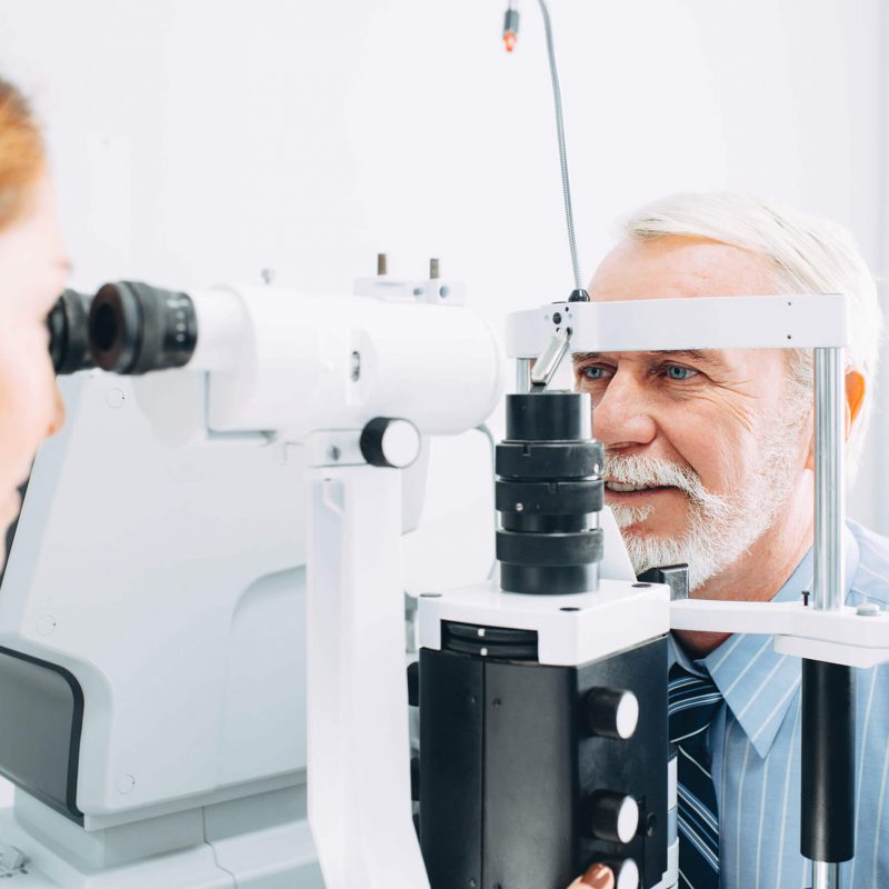 Senior man undergoing an eye exam with a slit lamp at an optometrist's office.