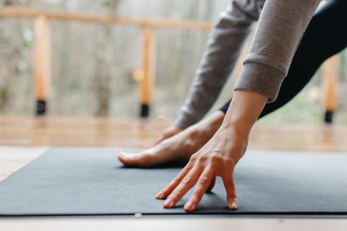 A person stretches their hand and foot on a yoga mat indoors, focusing on wellness