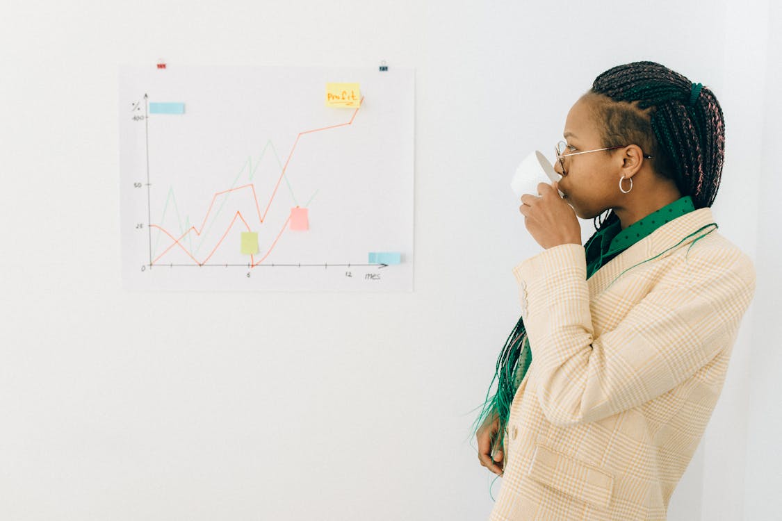 Professional woman in office attire drinking coffee while analyzing a financial graph indoors