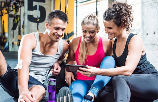 Group of smiling young people looking at cellphone in fitness club