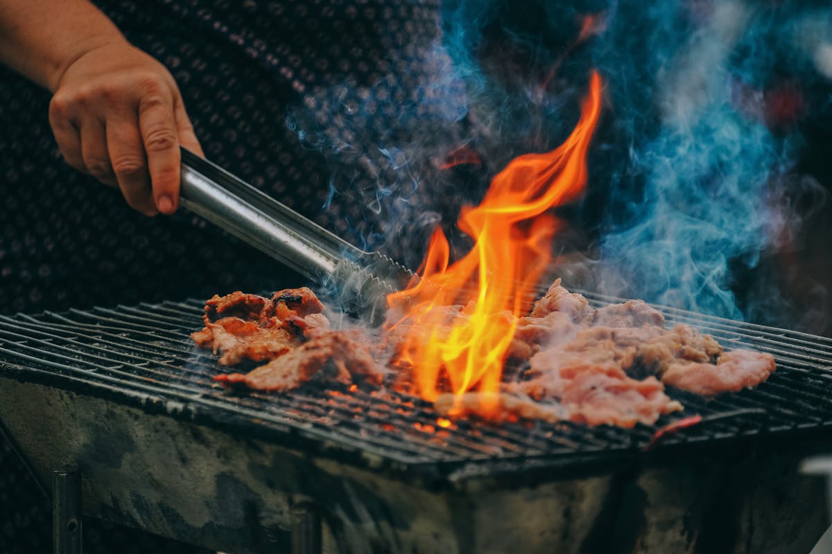 A private chef cooking meat on a grill with tongs