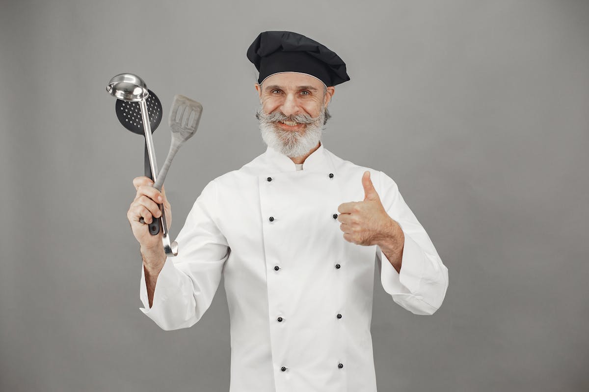 A private chef holding a bunch of utensils and giving a thumbs up