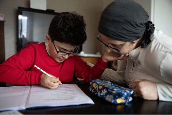 A patient sits at home with her son helping him with his homework.