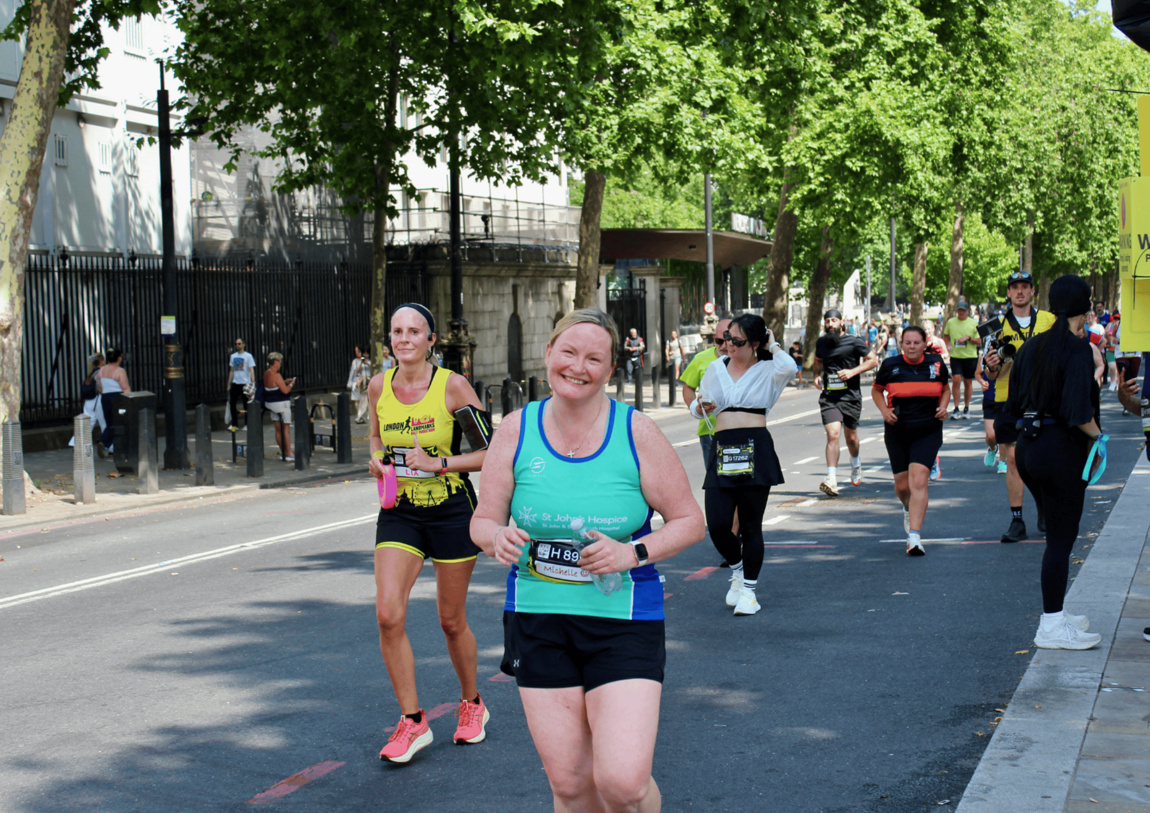 Runners wear green St John's green running vest. They hold up their finishers medal to the camera, smiling.