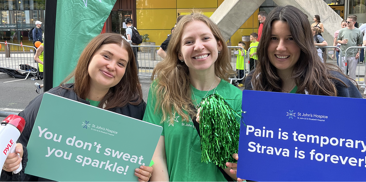 three women smiling and holding up supportive signs at a race