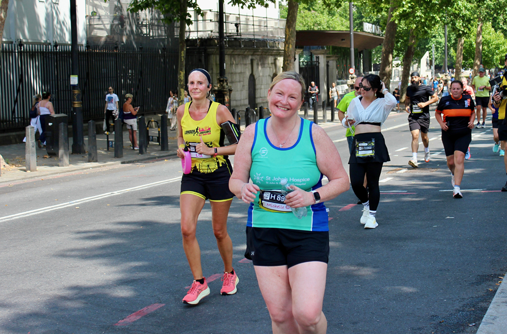 Runners wear green St John's green running vest. They hold up their finishers medal to the camera, smiling.