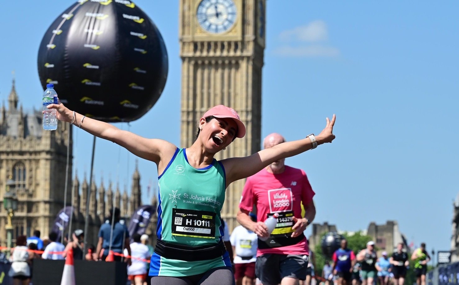 woman with green hospice vest, running with arms in the air & smiling 