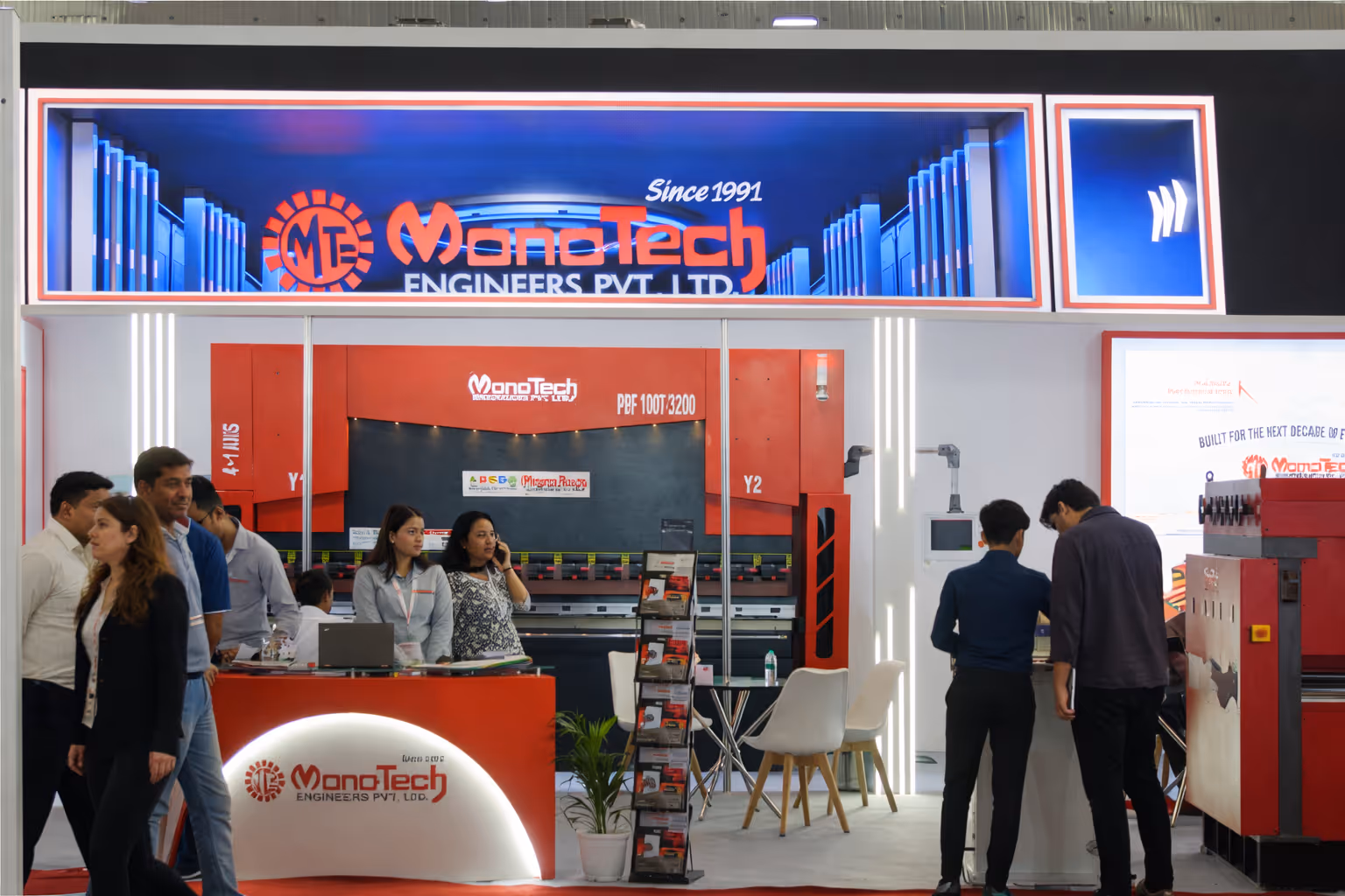 Trade show booth of MonoTech Engineers Pvt. Ltd. with people interacting and company machinery displayed.