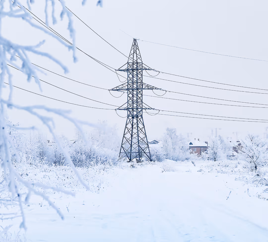 High-voltage electrical transmission tower in snowy winter landscape with power lines and frost-covered trees