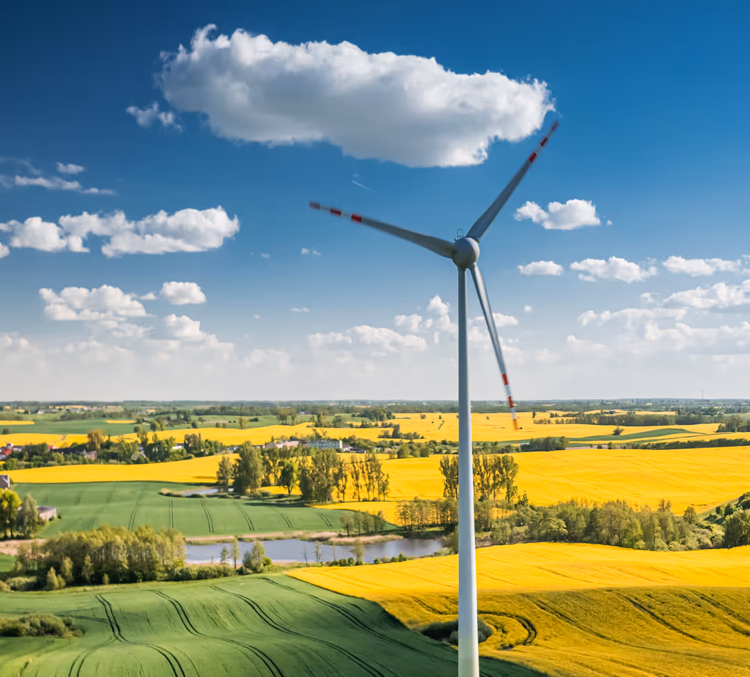 Wind turbine with red and white blades against blue sky overlooking patchwork of yellow canola fields and green farmland
